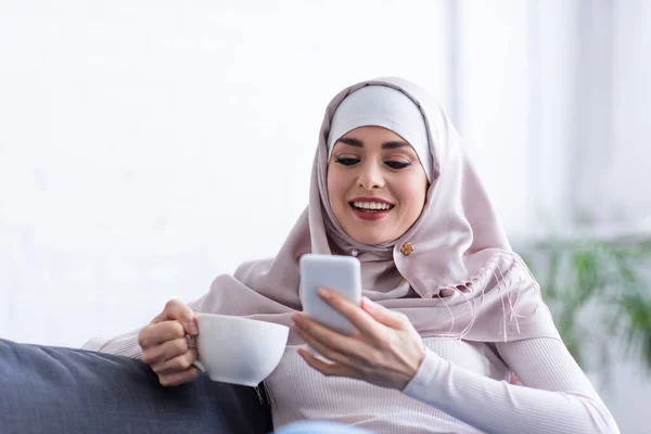 Mulher Muçulmana Alegre Segurando Xícara Chá Usar Telefone Móvel — Fotografia de Stock