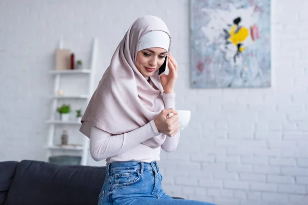 Mujer Árabe Sonriente Sosteniendo Una Taza Mientras Habla Por Teléfono — Foto de Stock