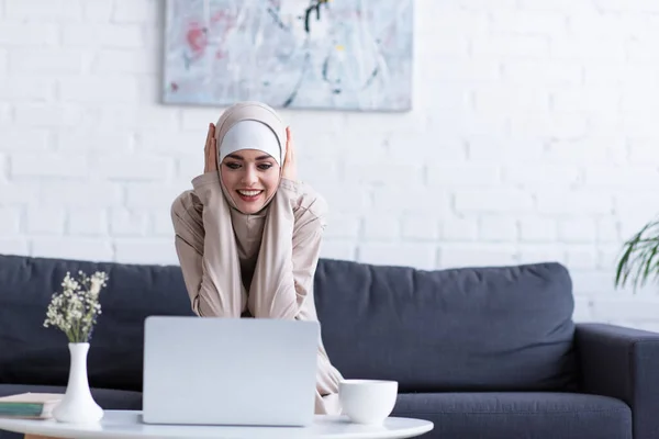Mulher Muçulmana Sorrindo Enquanto Olha Para Laptop Casa — Fotografia de Stock