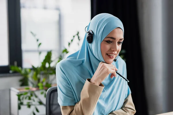 Mujer Árabe Positiva Hijab Auricular Que Sostiene Pluma Mientras Trabaja — Foto de Stock