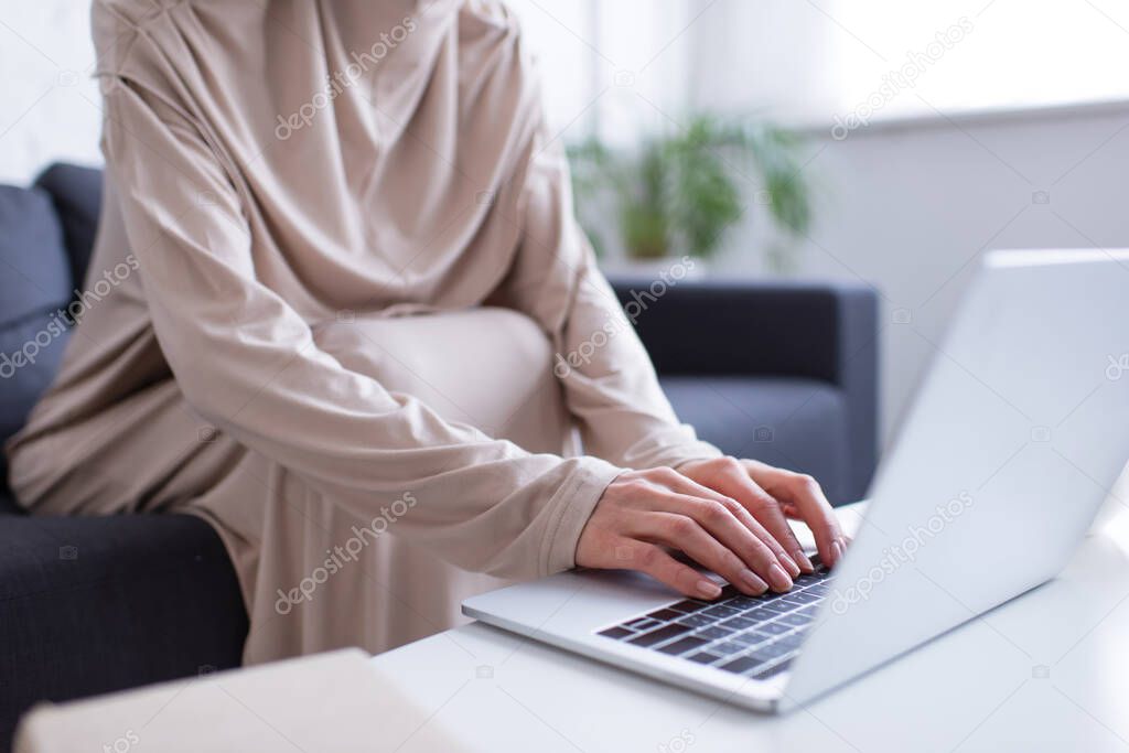 cropped view of muslim woman typing on laptop on blurred foreground