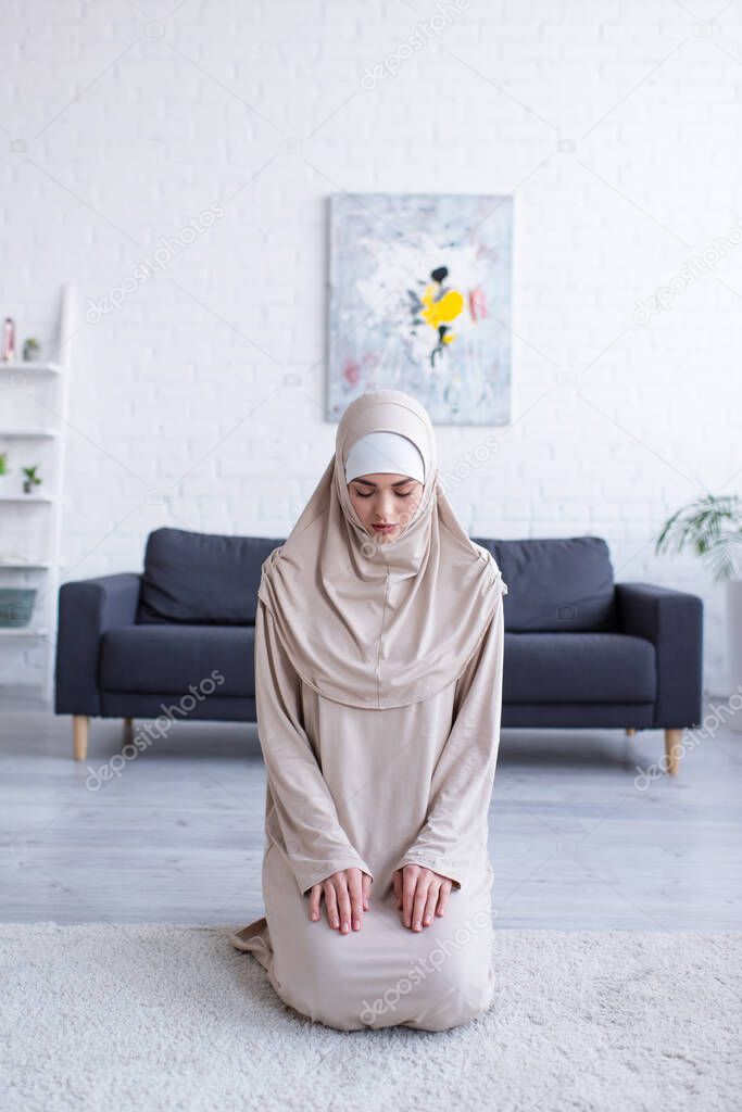 young muslim woman praying while sitting on floor with closed eyes