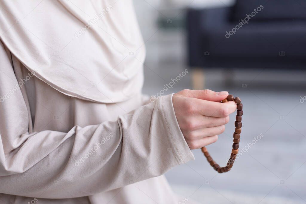 partial view of muslim woman with rosary praying at home