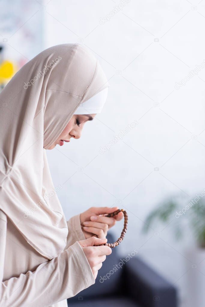 side view of arabian woman in hijab praying with closed eyes at home