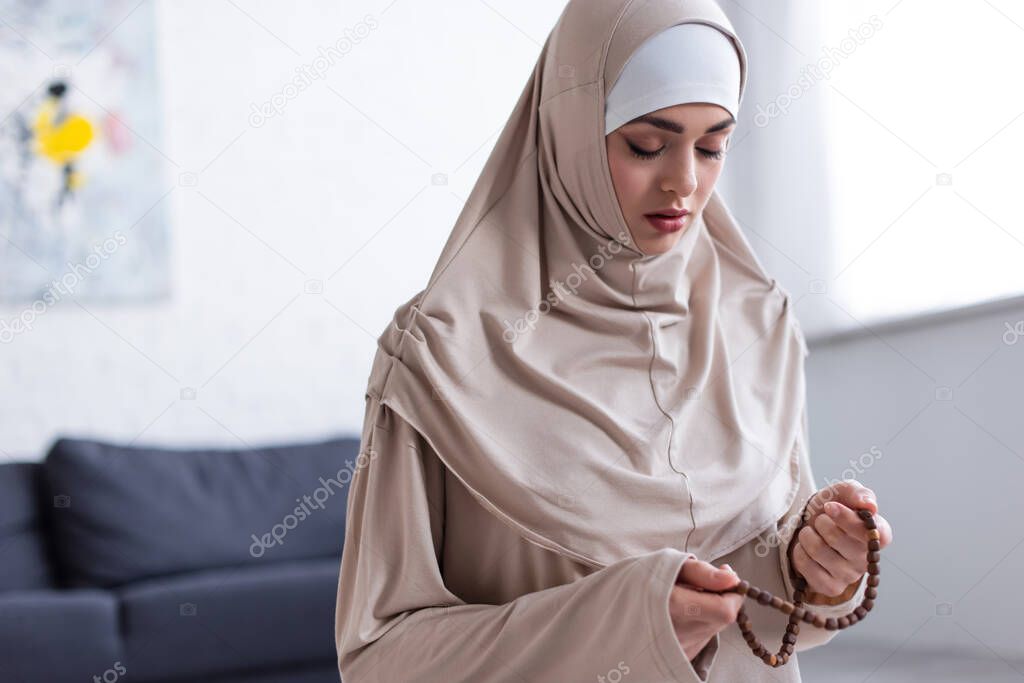 young muslim woman with rosary praying with closed eyes at  home