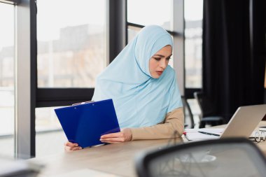 Güzel Müslüman iş kadını dizüstü bilgisayara bakarken pano tutuyor, ön plan bulanık