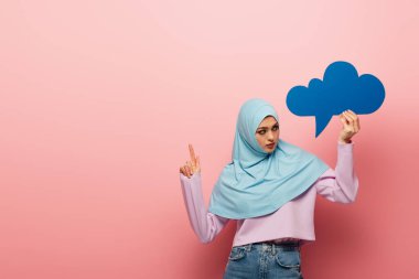 muslim woman with blue thought bubble pointing away with finger on pink background clipart