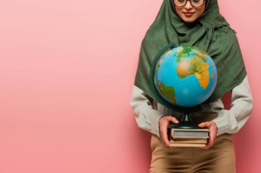 Küre tutan müslüman öğretmen ve pembe arkaplan üzerine ders kitapları