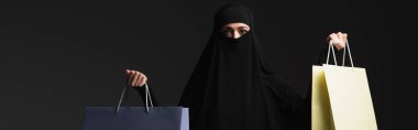 Siyah Niqab 'lı, siyah pankartta izole edilmiş çok renkli alışveriş torbalarıyla Arap bir kadın.