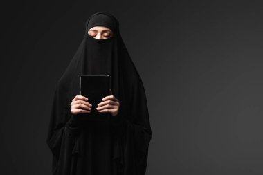 muslim woman holding koran while praying isolated on black clipart