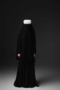 Siyah abaya 'daki Müslüman rahibenin tam boy görüşü ve siyah arka plandaki vr kulaklık.