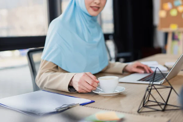 Laptop Yanında Çalışan Müslüman Kadını Görüşü Bulanık Önplanda Bir Fincan — Stok fotoğraf