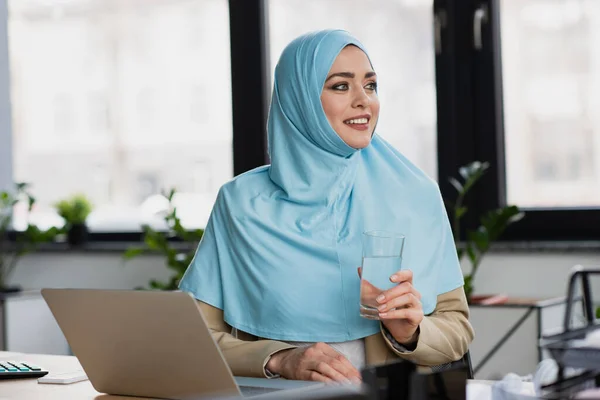成功的穆斯林女商人 拿着杯子 望着办公室里笔记本电脑旁边的远方 — 图库照片