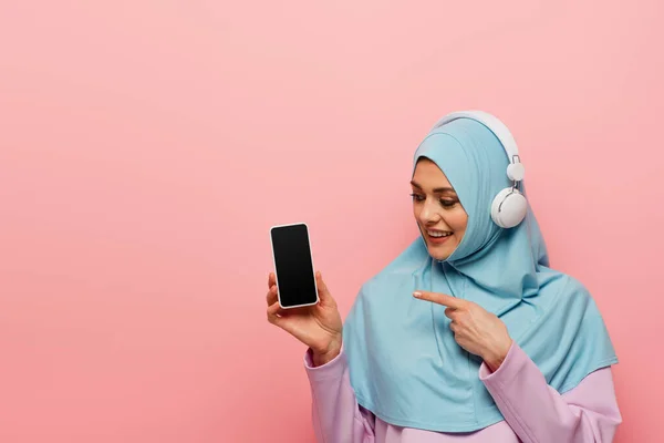 Smiling Muslim Woman Headphones Pointing Mobile Phone Blank Screen Isolated — Stock Photo, Image