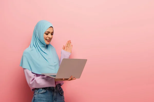 Alegre Mulher Muçulmana Acenando Mão Durante Chamada Vídeo Fundo Rosa — Fotografia de Stock
