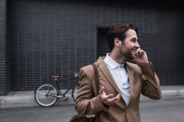 Resmi olarak mutlu genç işadamı dışarıda akıllı telefondan konuşuyor.
