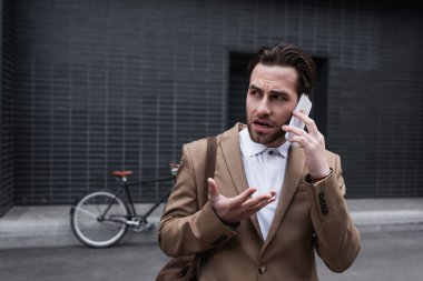 Stresli genç iş adamı dışarıda akıllı telefondan konuşuyor.