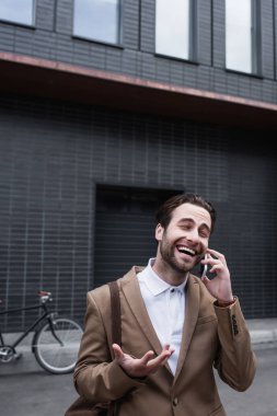 Resmi kıyafetli neşeli genç işadamı dışarıda cep telefonuyla konuşuyor.