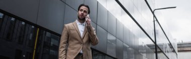 İş adamı binanın yakınında cep telefonuyla konuşuyor, afiş