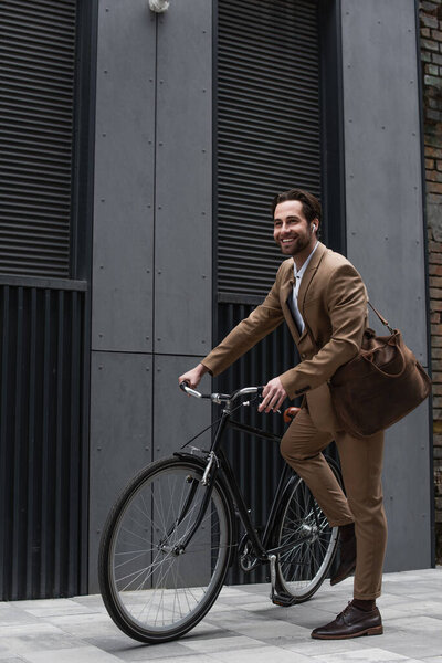 full length of happy businessman in earphones riding bicycle 