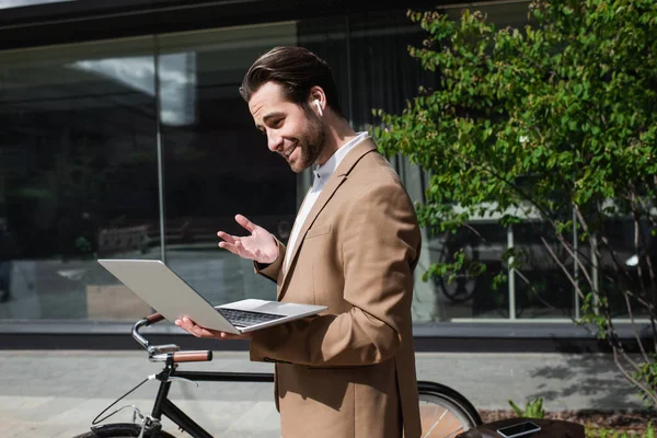 happy businessman in earphones having video call on laptop outside