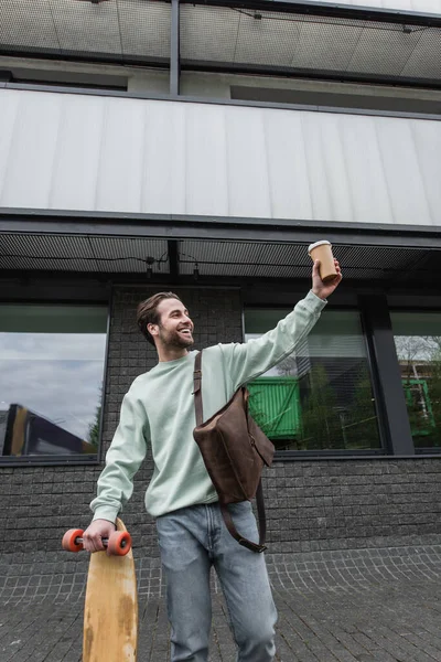 Sonriente Hombre Sudadera Sosteniendo Taza Papel Longboard Fuera — Foto de Stock