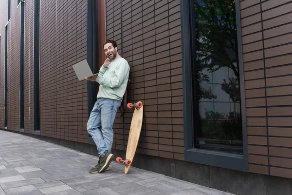 Užaslý Volné Noze Mikině Bezdrátových Sluchátkách Držící Notebook Ukazující Prstem — Stock fotografie