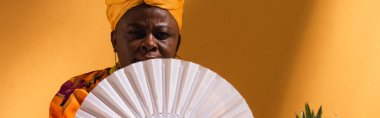 Ciddi orta yaşlı Afro-Amerikalı kadın yüzünü turuncu ve afiş ile kapatıyor.