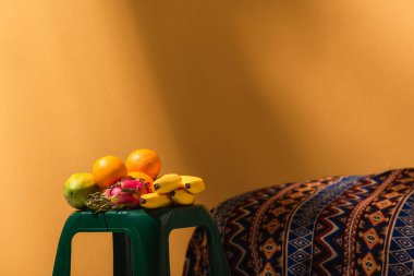 Portakallı süs battaniyesinin yanındaki taburede egzotik meyveler
