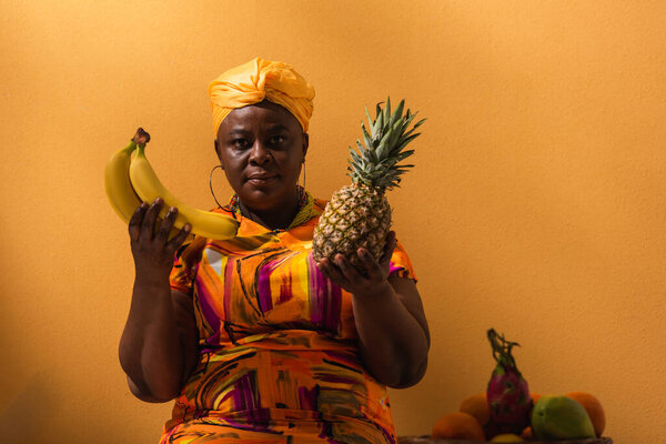 Африканская женщина средних лет держит ананас и бананы рядом с фруктами на апельсине