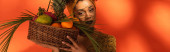 mladá africká americká žena držící koš s exotickým ovocem blízko obličeje na pomeranči, prapor