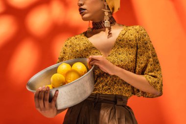 Sarı bluzlu Afro-Amerikan kadının portakallı limonlu metal kâse tutuşu.