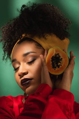 Gözleri kapalı genç Afrikalı Amerikalı kadının portresi. Elinde papaya 'nın yarısı yeşil ellerde.