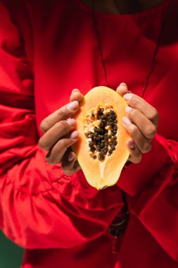 Kırmızı bluzlu Afrikalı Amerikalı genç bir kadının elindeki papaya 'nın yarısının görüntüsünü kapatın.