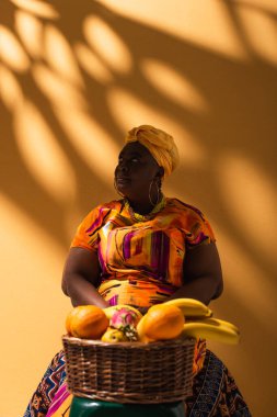 Orta yaşlı Afrikalı Amerikalı satıcı, portakallı meyvelerin yanında oturuyor.