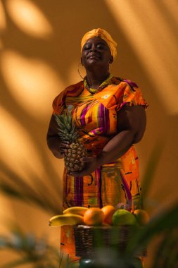 Portakallı ananaslı meyvelerin yanında duran kendinden emin Afro-Amerikan satış elemanı.