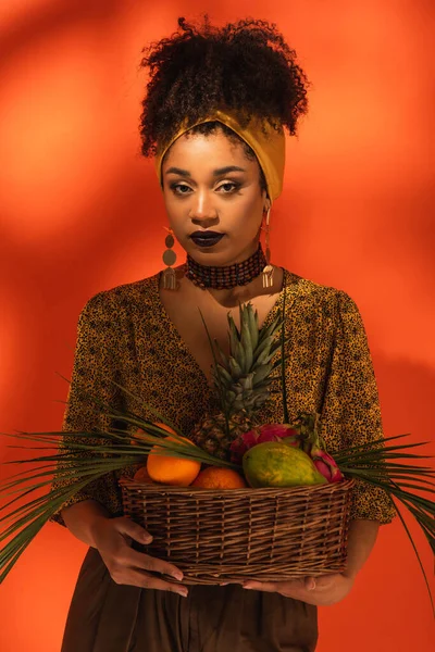 若いアフリカ系アメリカ人の女性がオレンジにエキゾチックな果物のバスケットを持っています — ストック写真
