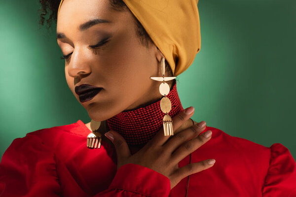 молодая африканская американка в платке касающаяся шеи с закрытыми глазами на зеленом