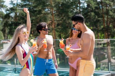 Young interracial friends in sunglasses and swimwear spending time at resort  clipart