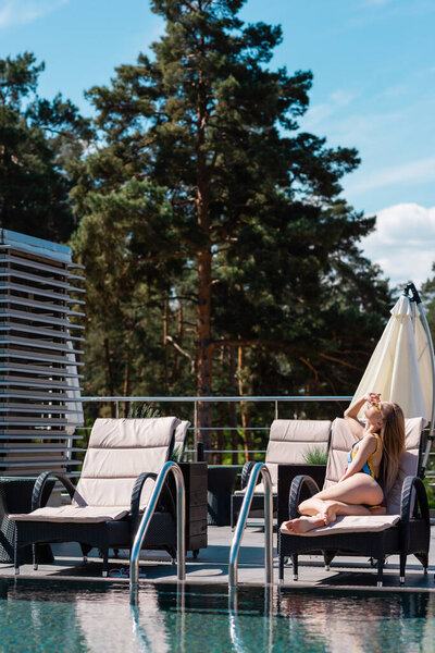 Side view of woman in swimwear lying on deck chair near swimming pool 