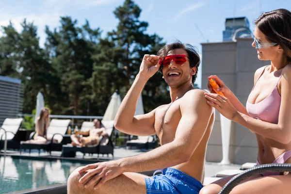 Lächelnde Frau Badeanzug Mit Sonnencreme Der Nähe Von Freund Und — Stockfoto