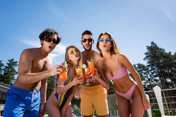 Low angle view of excited multiethnic friends holding cocktails at resort 