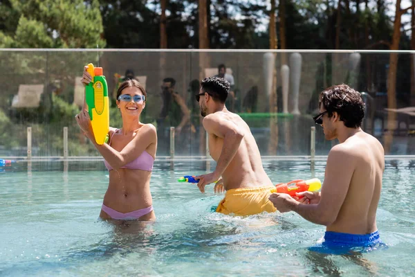Cheerful Woman Playing Water Gun Multiethnic Friends Swimming Pool — Stock Photo, Image