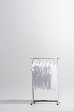 collection of stylish t-shirts hanging on clothes rack isolated on grey  clipart
