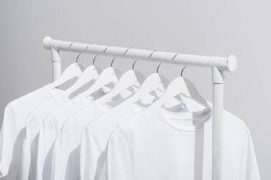 collection of trendy white t-shirts hanging on clothes rack isolated on grey  clipart