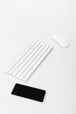 Bilgisayar faresi ve klavye yakınındaki boş ekranlı akıllı telefon beyaz ekranda izole edildi 