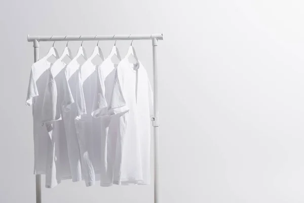 collection of white t-shirts hanging on clothes rack isolated on grey