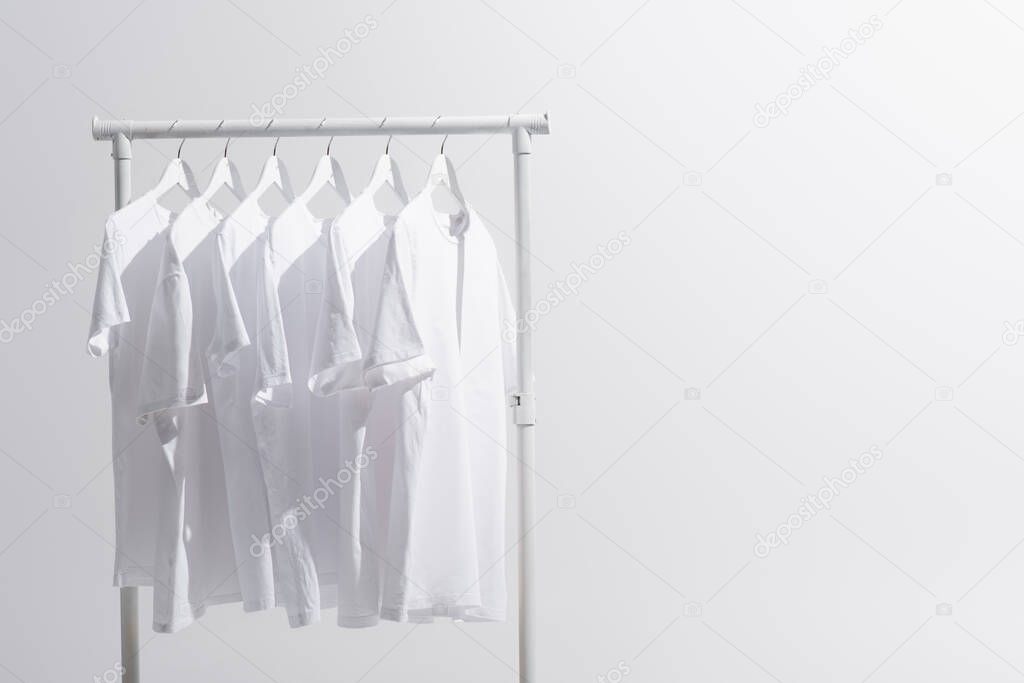 collection of white t-shirts hanging on clothes rack isolated on grey 
