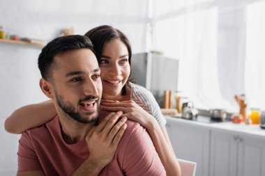 Tişörtlü pozitif genç çift mutfakta nazikçe sarılıyorlar.