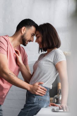 Genç aşıklar modern mutfakta birbirlerine sarılıp dokunuyorlar.